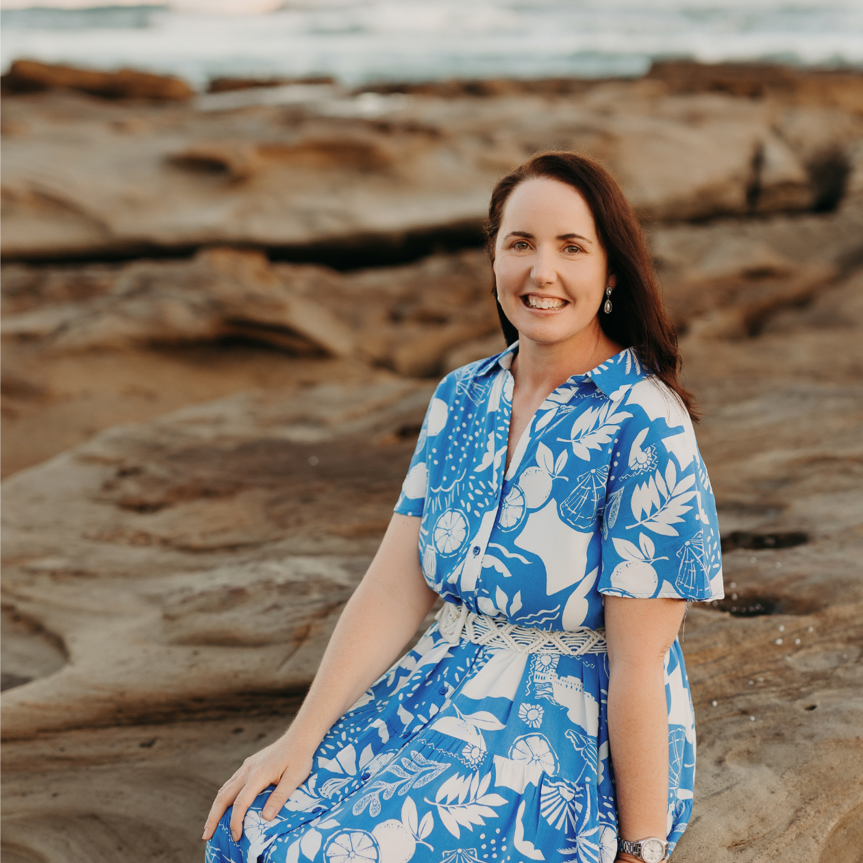 Freelance SEO copywriter Jane Havercroft sits on rocks at her local beach, smiling at the camera